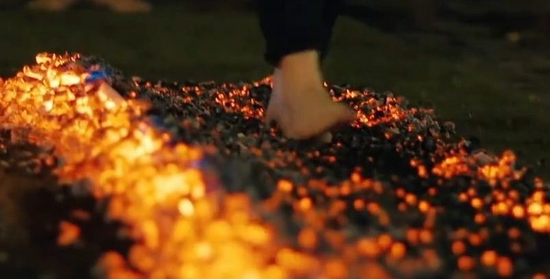 Close-up of bare feet stepping onto glowing birch embers, representing the somatic shift from hesitation to certainty during a Kick Ash firewalk.